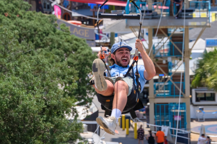 Person zip-lining with a joyful expression in an urban area.