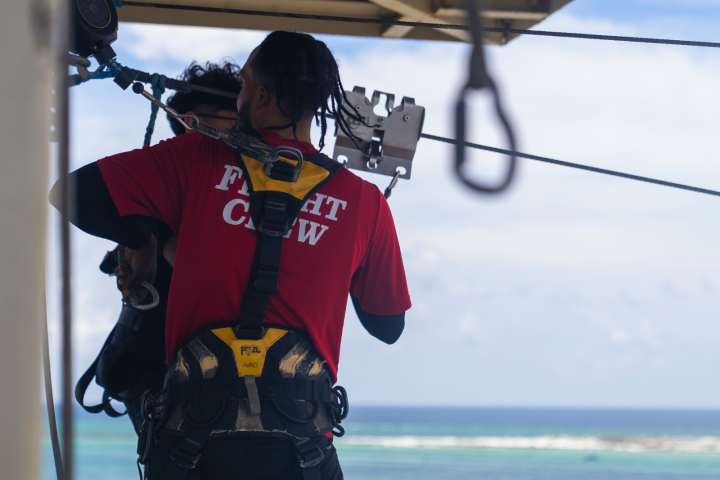 Person in red 'Flight Crew' shirt attaches harness to cable over water.